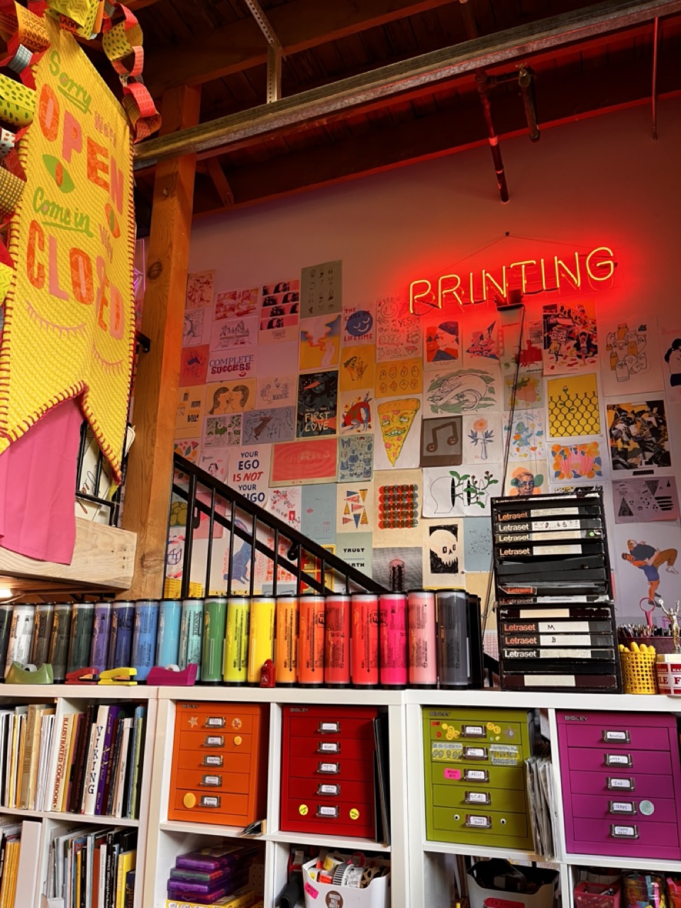 interior of Outlet, featuring a wall of prints, handmade banner, and a bookshelf full of riso ink and supplies
